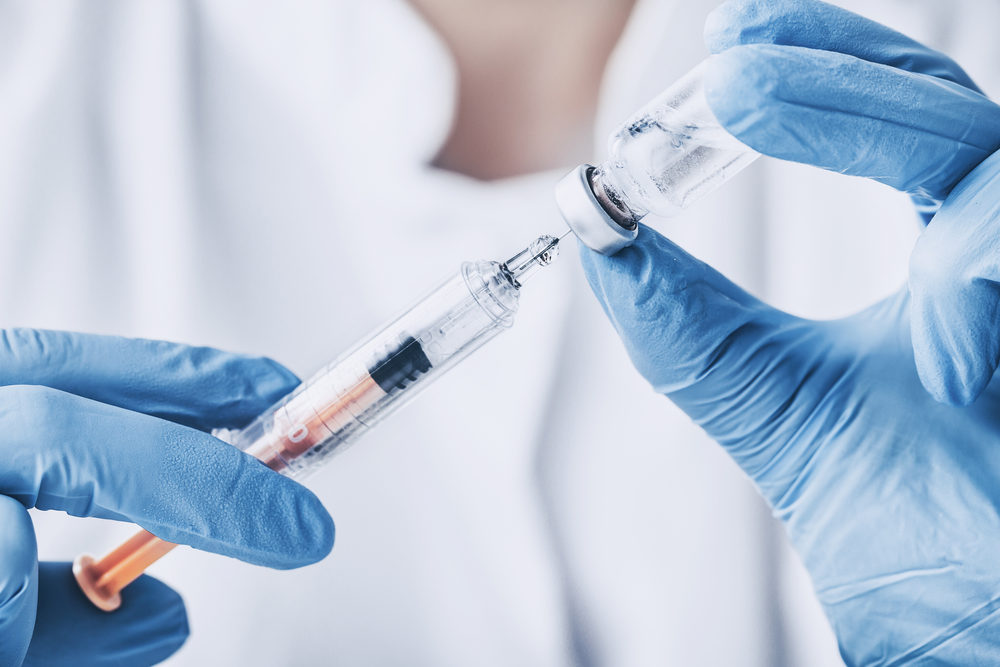 Blue gloved hands fill an injection needle from a clear vial