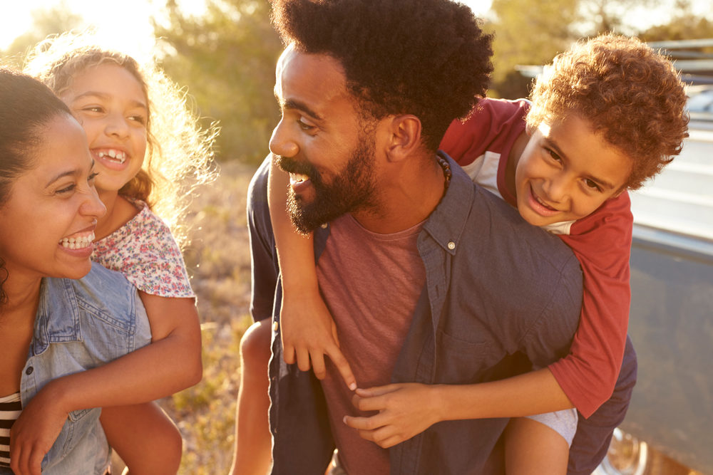 Selling Again? Get More for Your Structured Settlement Payments Happy parents giving kids piggyback rides outside in the sunshine.