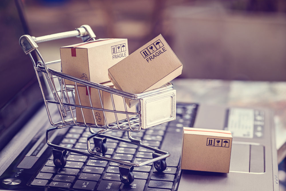 A tiny shopping cart overflowing with shipping boxes on a laptop keyboard