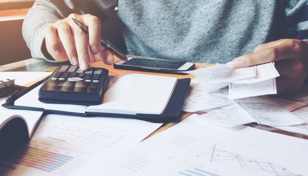 A man punching numbers into a calculator while holding a stack of bills