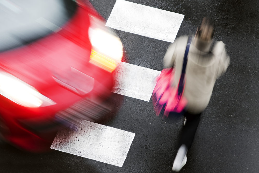 A red car about to strike a pedestrian at a crosswalk, as seen from above