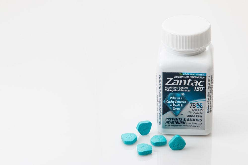 A bottle of Zantac 150 with some blue pills beside it, on a white background