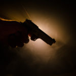 Silhouette of a man\'s hand holding a smoking handgun