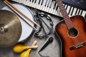 Musical instruments on a concrete floor: drums, guitar, keyboard, tambourine, and maracas