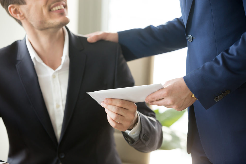 A businessman hands another man a stuffed white envelope