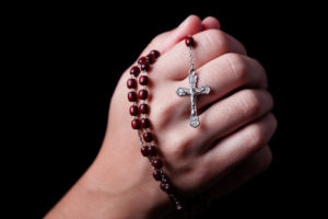 Rosary beads clutched in two hands together in prayer