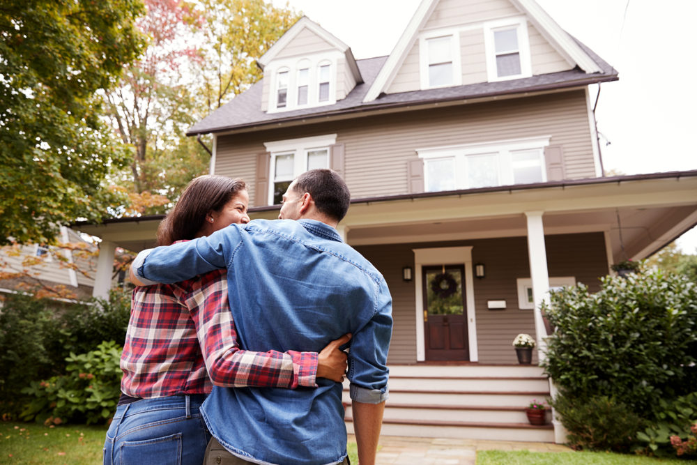 A couple embraces in front of a large house