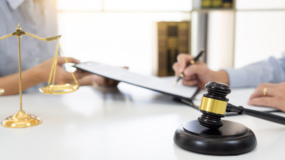 lawyer signing contract at desk with gavel and scales in foreground