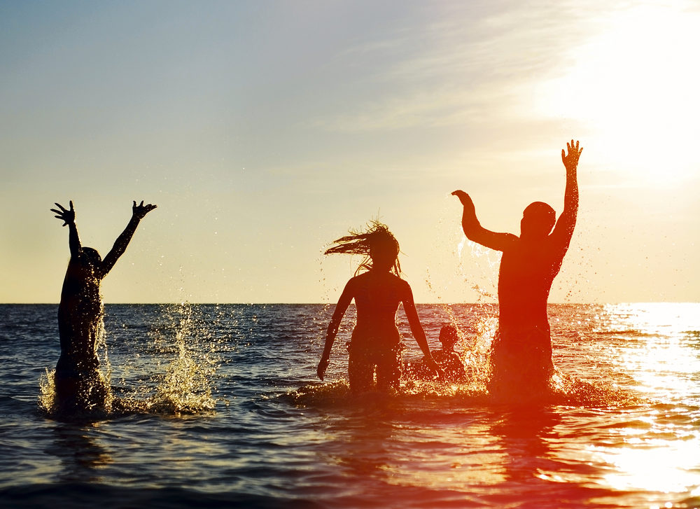 Silhouettes of young group of people jumping in ocean at sunset