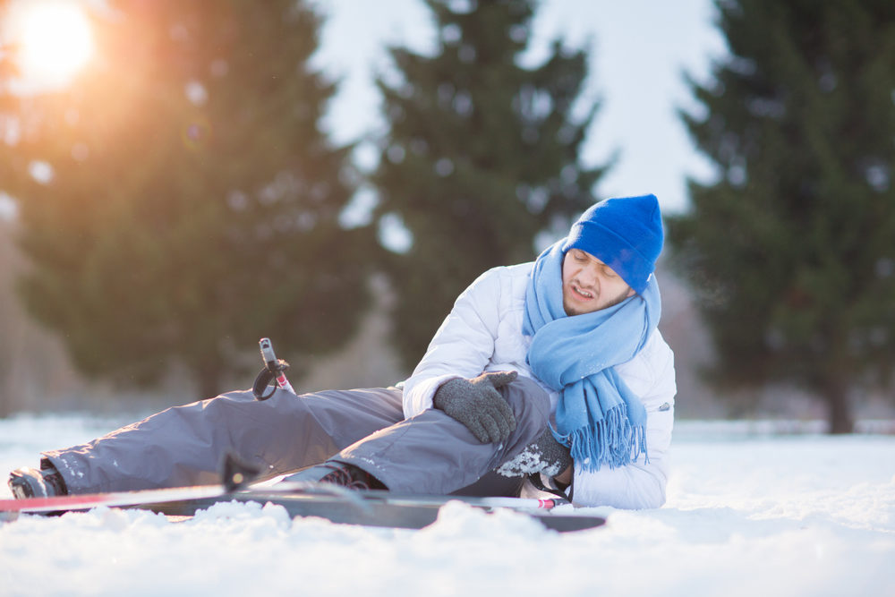 Young sportsman rubbing his hit knee after crash in snow during ski training