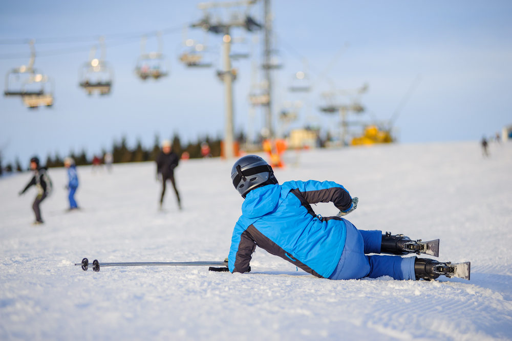 Young woman skier in blue ski suit after the fall on mountain slope trying get up against ski-lift. 