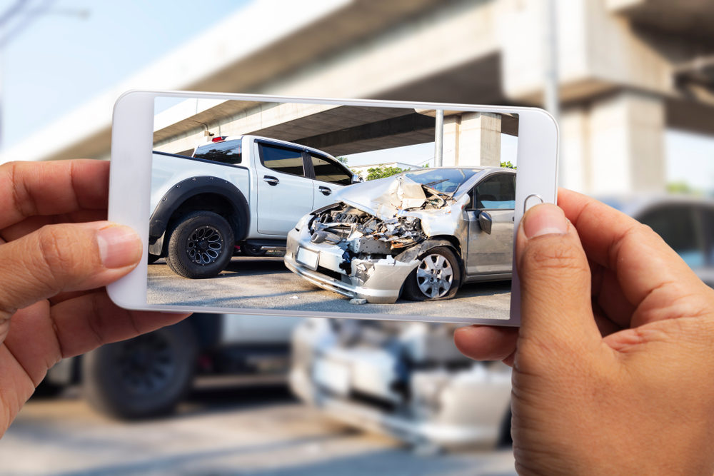 Car insurance agents take pictures of car accident-damaged vehicles with a smartphone as a proof of insurance claim.