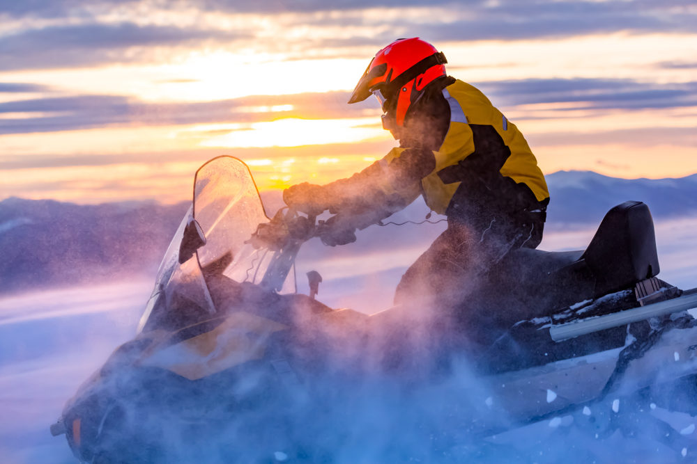 A man is riding snowmobile in mountains. 