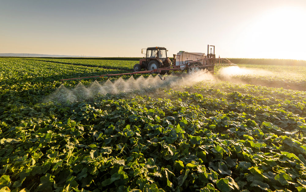 Tractor spraying pesticides on vegetable field with sprayer at spring