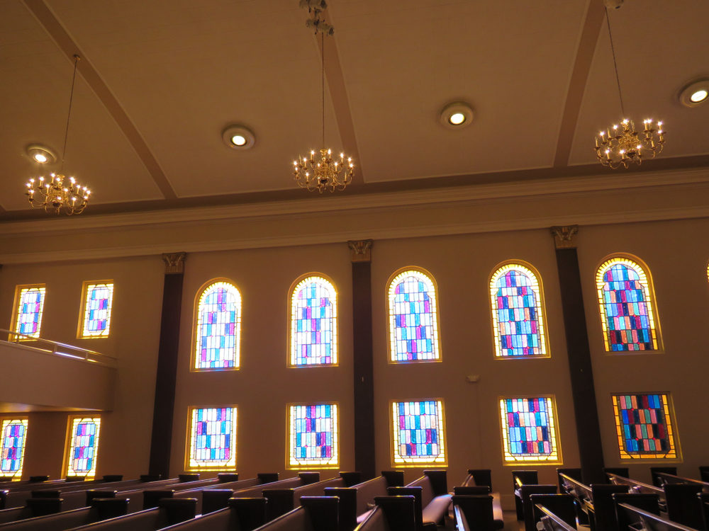 Stained Glass wall behind rows of pews inside a church.