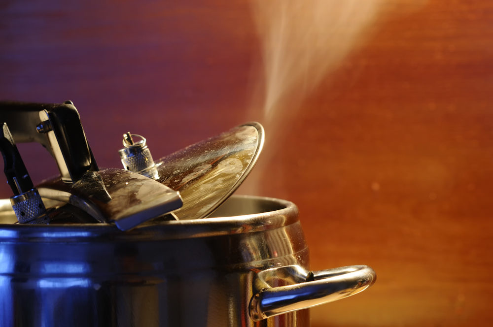 Steam escaping from lid of pressure cooker with reflection of modern kitchen.