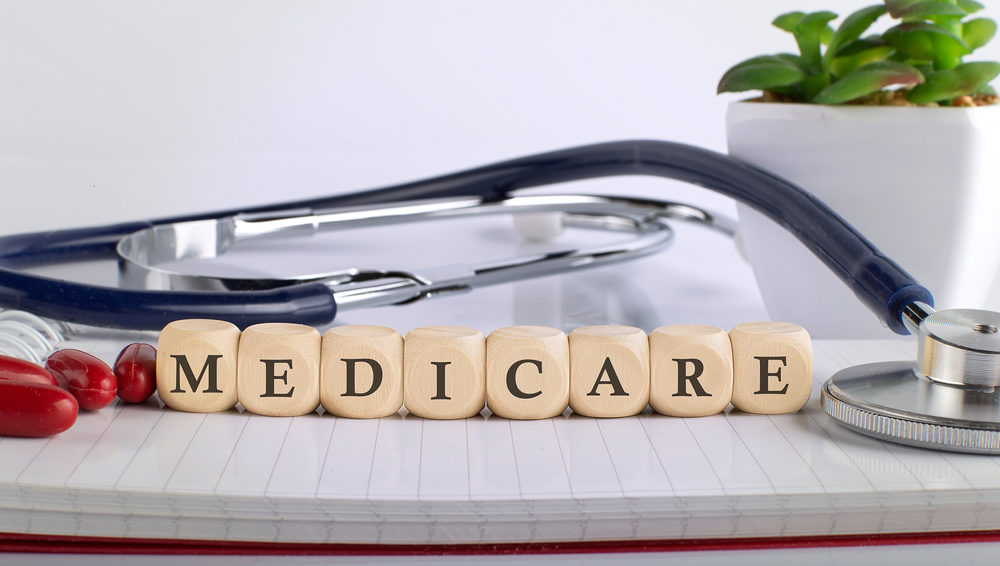 notepad with blocks spelling out medicare with a plant and a stethoscope