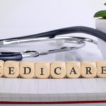 notepad with blocks spelling out medicare with a plant and a stethoscope