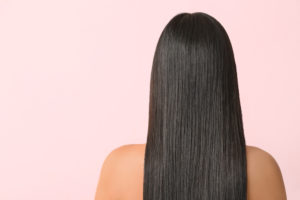 back view of long straight brunette hair on a female with a pink background