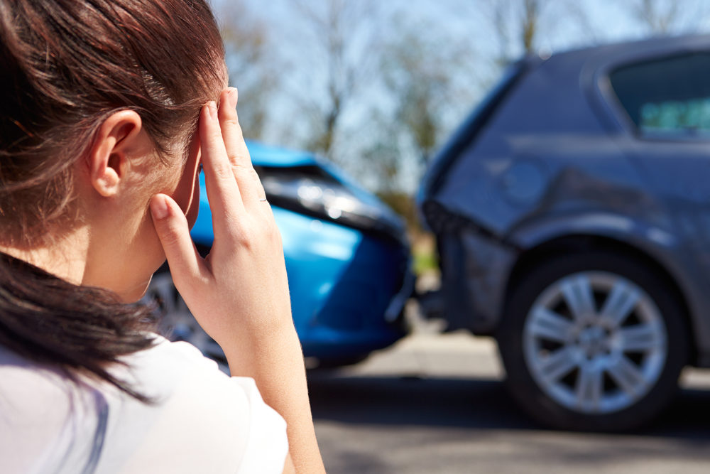 Stressed Female Driver Sitting At Roadside After Traffic Accident holding her head