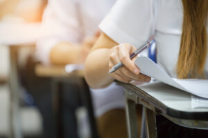 closeup of a female student taking a test at desk with blurred students behind
