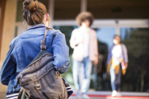 rear view of female student walking toward campus with blurred students in background