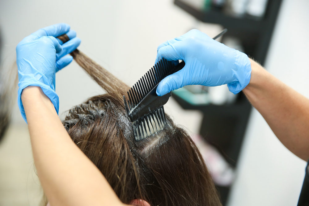 gloved hands of a hairstylist applying hair dye to female in salon