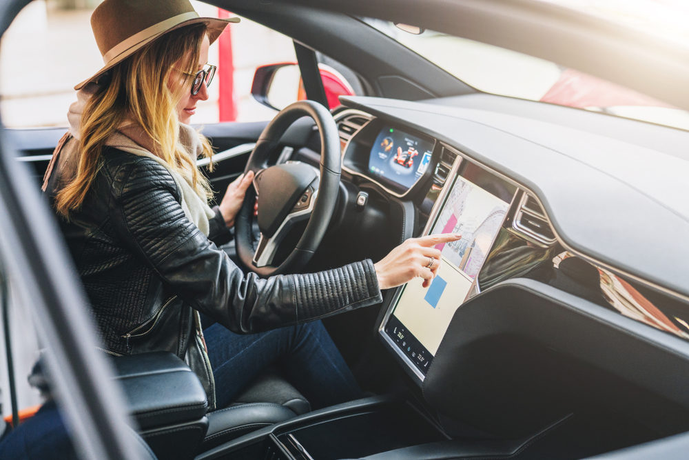 Young woman sits behind wheel in car and uses an electronic dashboard