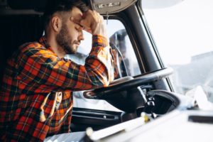 fatigued male trucker resting his elbows on the wheel while holding his forehead from exhaustion