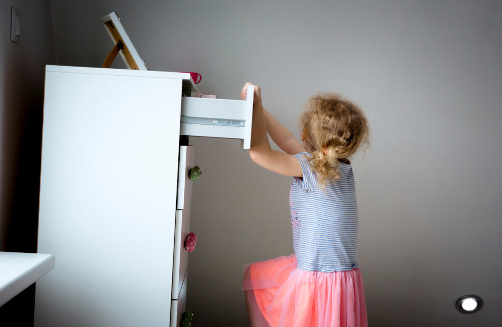 Young girl climbing on modern high dresser furniture,