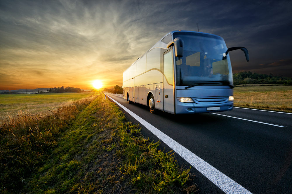 A transport bus drives down a rural roadway at sunset