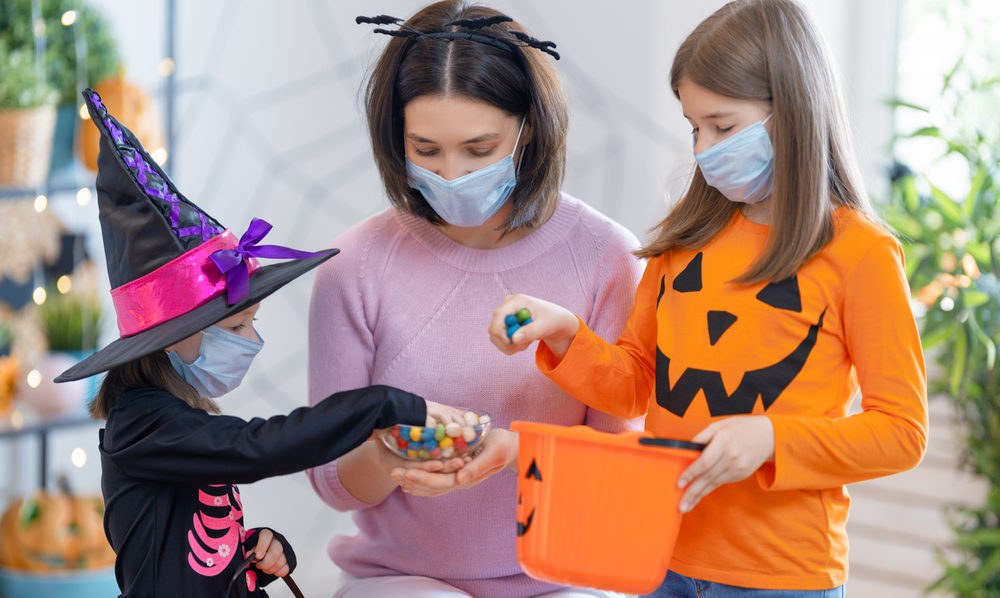 Halloween Safety Tips Happy family celebrating Halloween. Mother and children wearing face masks protecting from COVID-19.