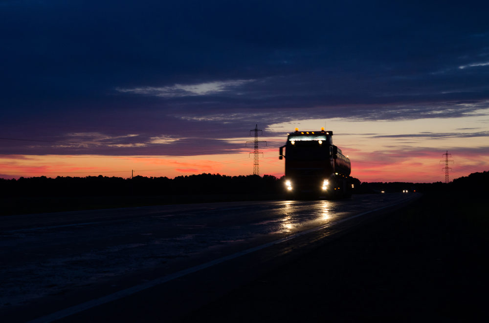 Silhouette of a big rig driving down the highway at nighttime