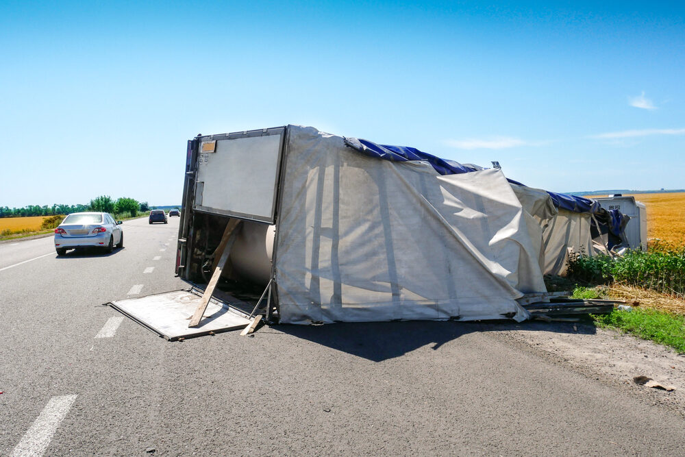 cars passing an overturned truck on the highway