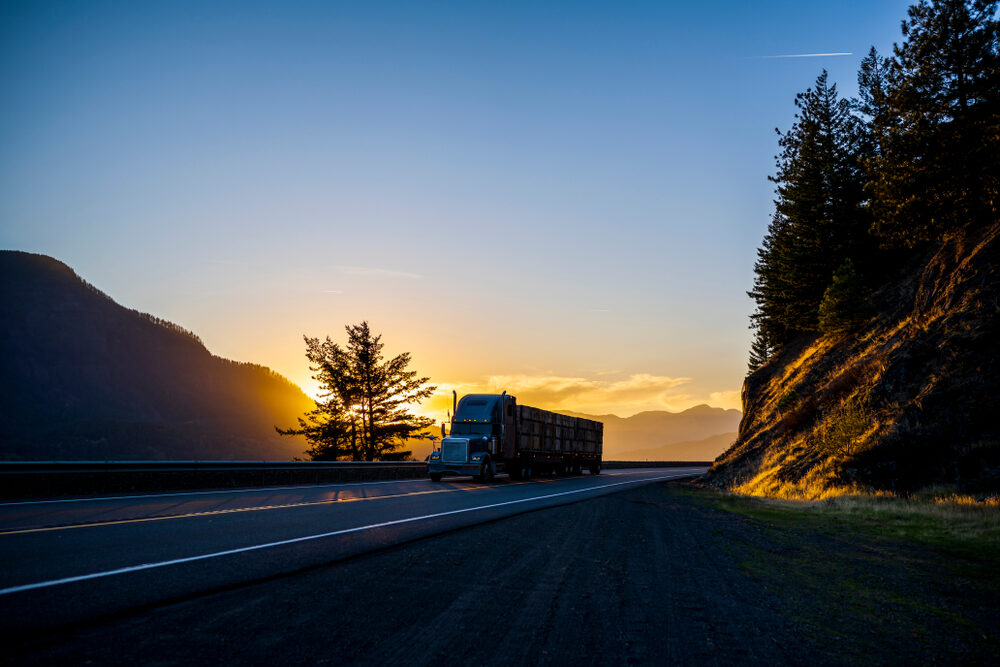 semi truck transporting cargo on highway through mountains at sunset
