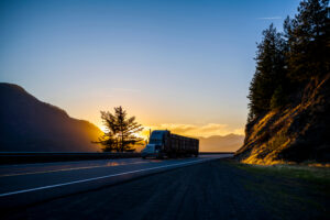 semi truck transporting cargo on highway through mountains at sunset