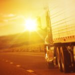 semi truck driving on road towards sun