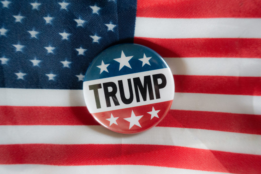 A campaign button with TRUMP printed on it rests on an American flag