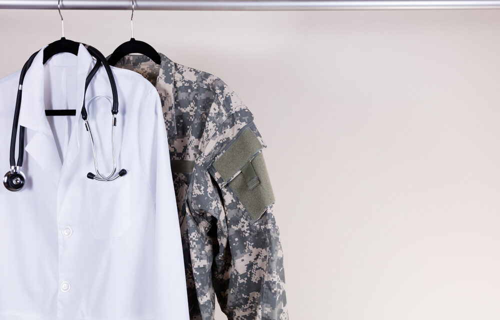 Doctor Charged in One of the Military’s Largest Sexual Abuse Cases Medical Doctor Consultation white coat, stethoscope around collar, and military uniform hanging on rack.