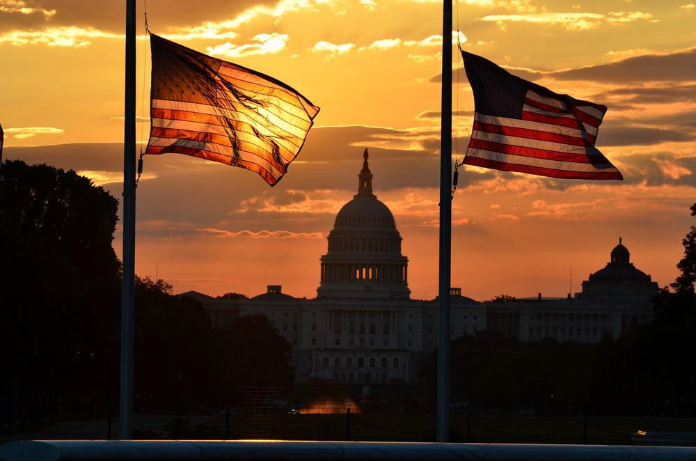 United States Capitol building silhouette and US flags at sunrise - Washington DC