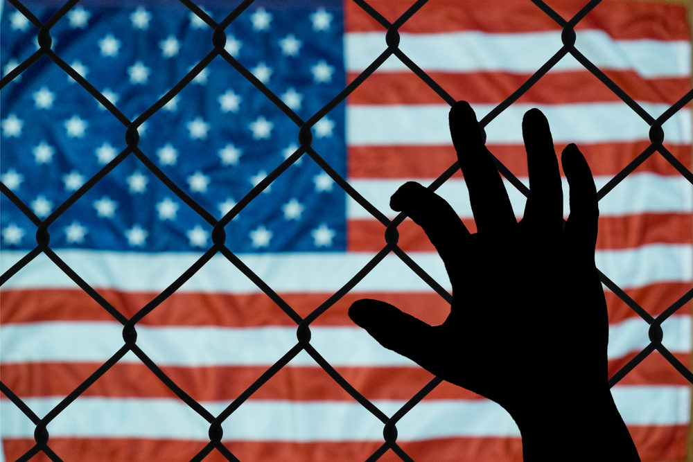Should Good People Get a Little Dirty Silhouetted hand grasping a chain-link fence with American flag on the other side