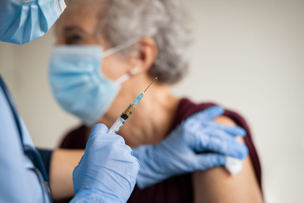 Close up of general practitioner hand holding vaccine injection while wearing face protective mask during covid-19 pandemic. 