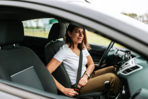  woman sitting in a car putting on her seat belt.
