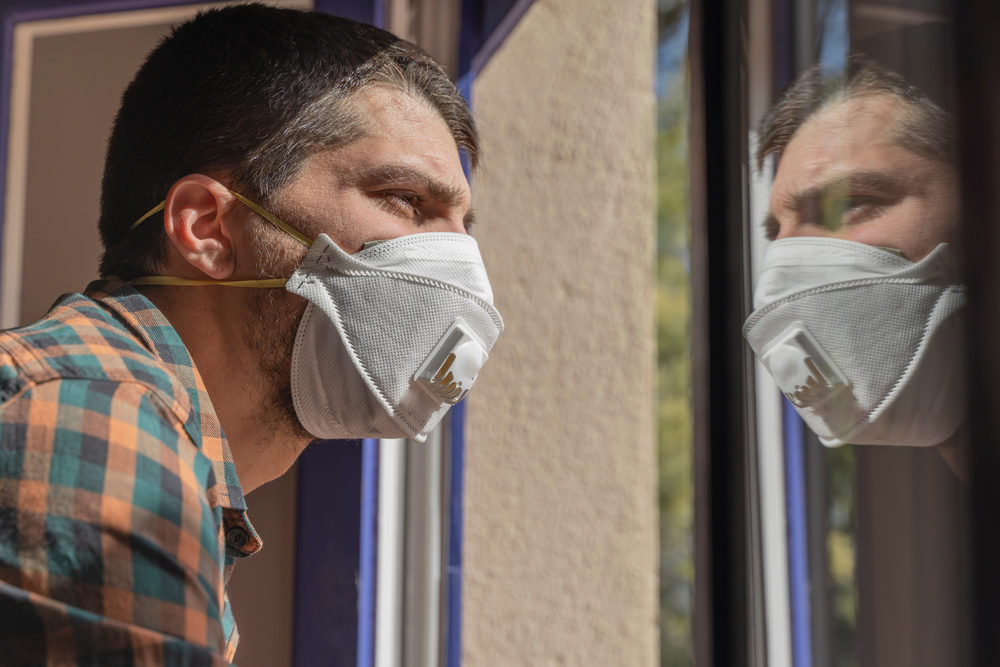 A facemask-wearing man peers out the window