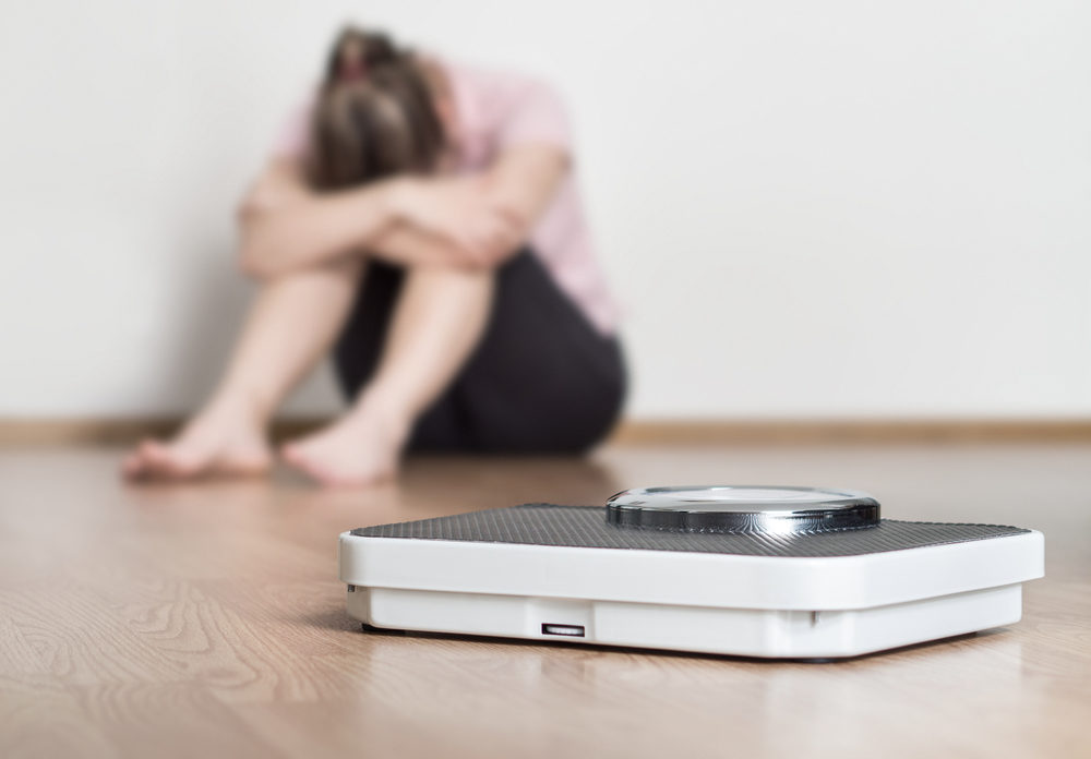A bathroom scale on the floor with an upset woman in the background