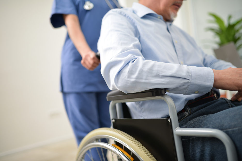 nurse assisting an elderly male in  a wheelchair