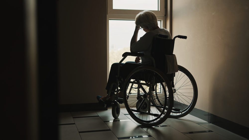 Are Nursing Home Laws Protecting Seniors? lonely senior woman looking through the window of the nursing home.