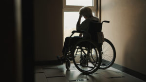 lonely senior woman looking through the window of the nursing home.
