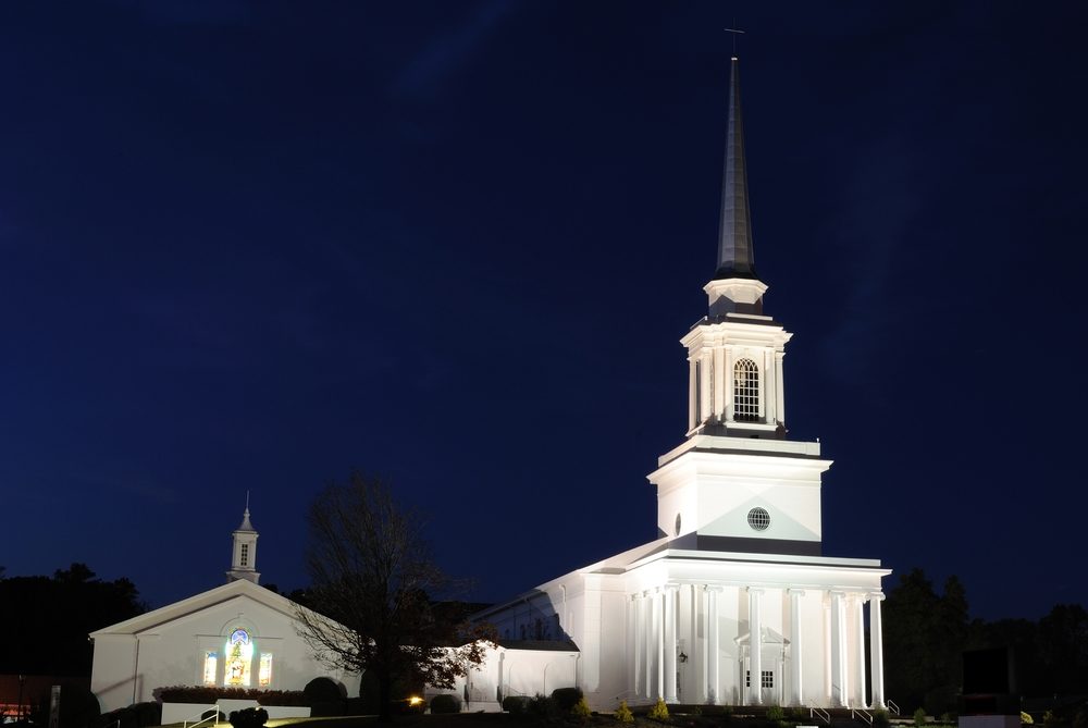 white church lit up at night with dark sky in background