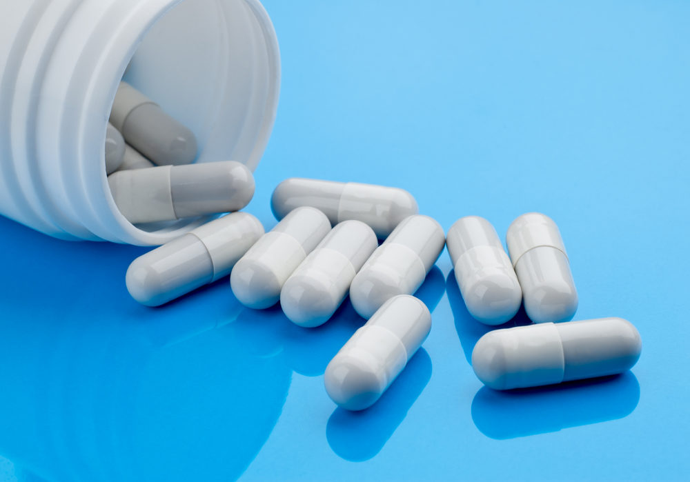 White pill capsules spilling onto a blue table from a bottle